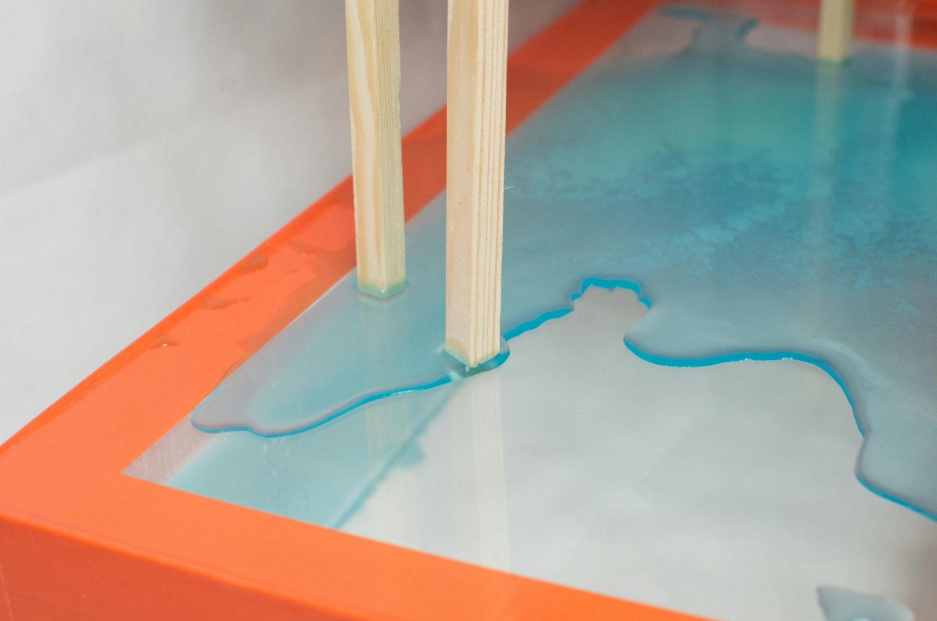 A vibrant minimalist artwork featuring a turquoise acrylic spill on a wooden structure.