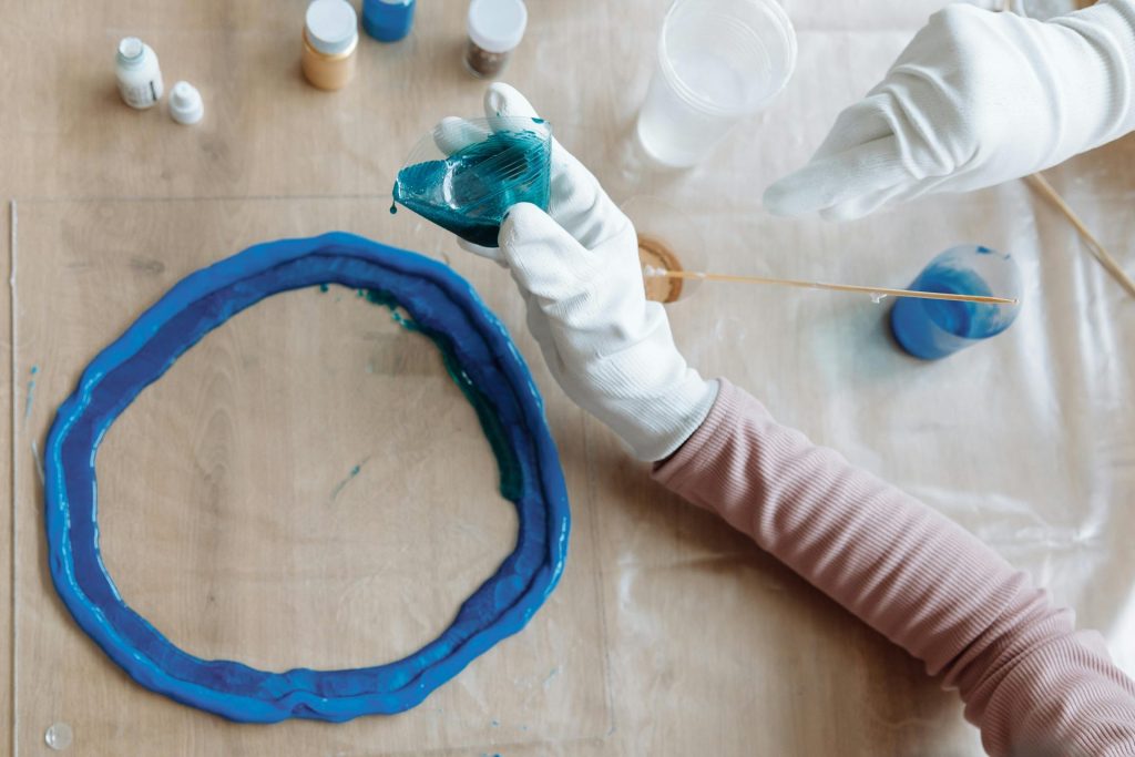 Close-up of hands crafting blue resin art indoors, showcasing artistic process.
