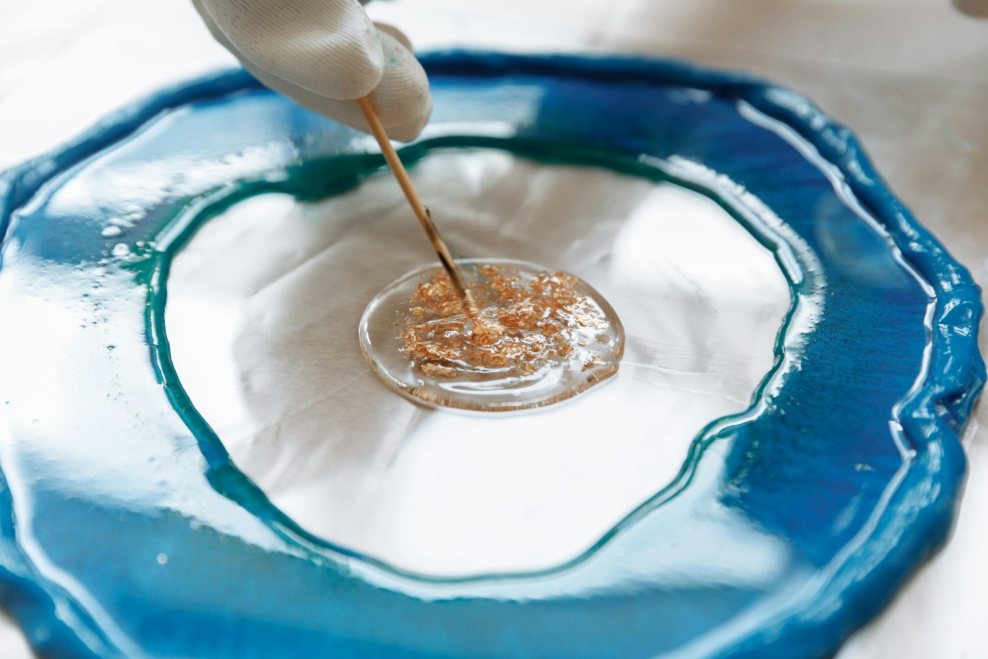 Close-up of a hand crafting intricate resin art with blue and gold details.