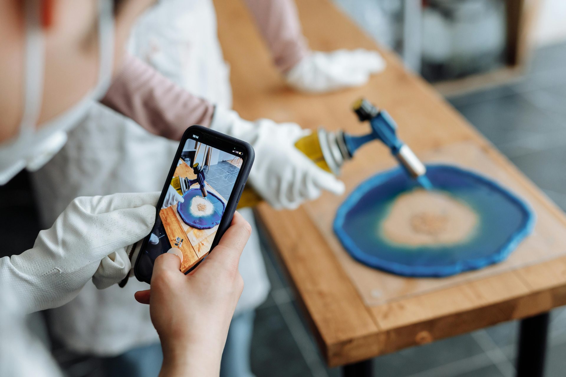 Close-up of a person photographing a resin art piece being crafted with a blowtorch.